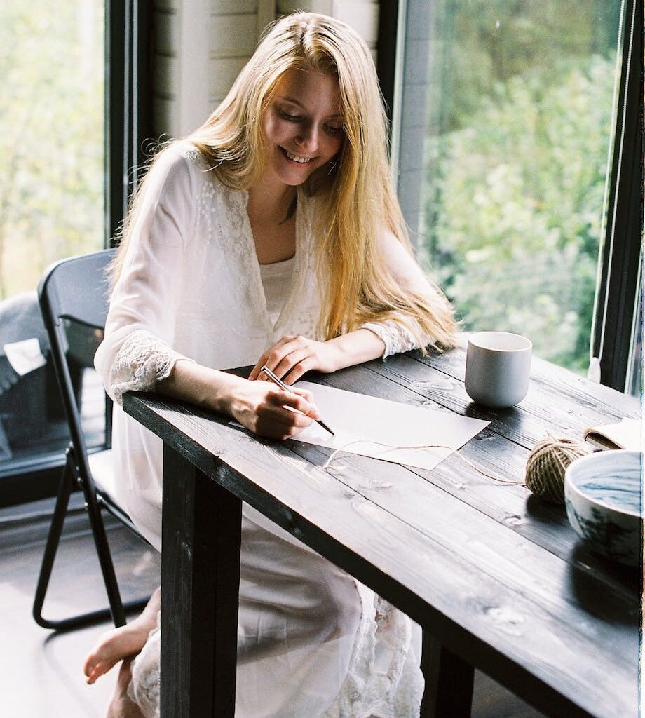 smiling barefooted lady writing thoughts on paper at home